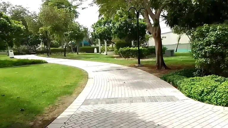 Извилистая пешеходная дорожка из светлого кирпича, проходящая через зеленые газоны, ухоженные кустарники и деревья парка Zabeel.