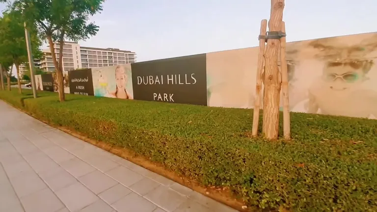 Темные силуэты зданий и деревьев района Dubai Hills на фоне яркого оранжевого неба во время заката.