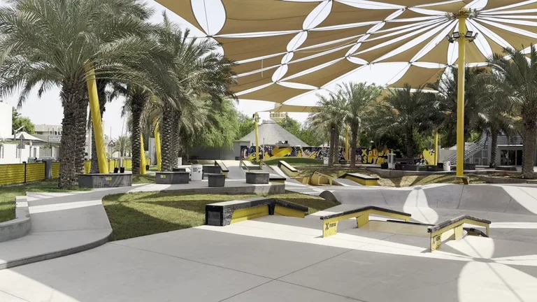 Современный скейт-парк на Kite Beach с бетонными рампами под большим навесом от солнца среди пальм.