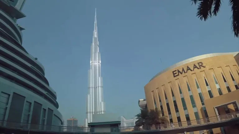 Вид снизу на небоскреб Бурдж-Халифа, возвышающийся над зданием Emaar в комплексе Dubai Mall и пальмами.